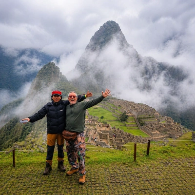 Two travelers posing with Machu Picchu and misty Andean mountains in the background during a scenic visit in Peru | Inca Culture Travel