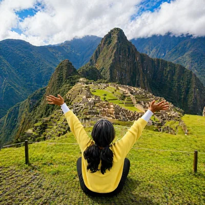 Woman raising her arms while admiring the iconic Machu Picchu citadel on the Short Inca Trail, Peru | Inca Culture Travel
