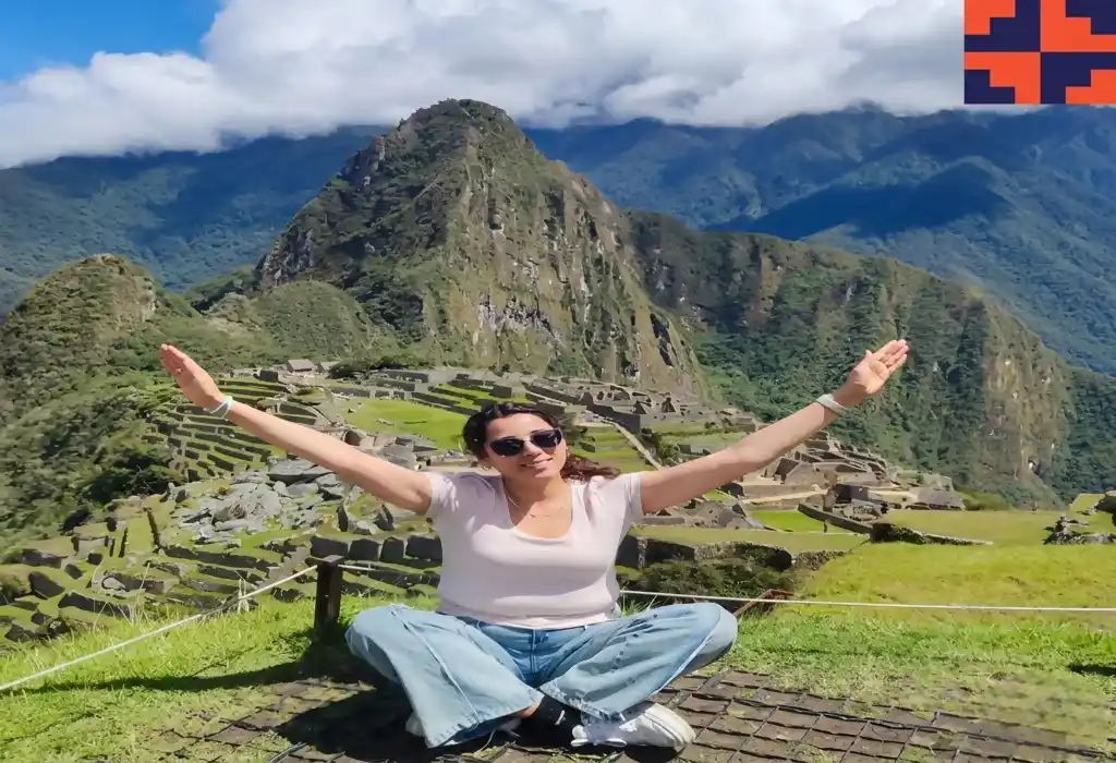 Woman sitting on the grass overlooking Huayna Picchu mountain and the ancient ruins of Machu Picchu | Inca Culture Travel